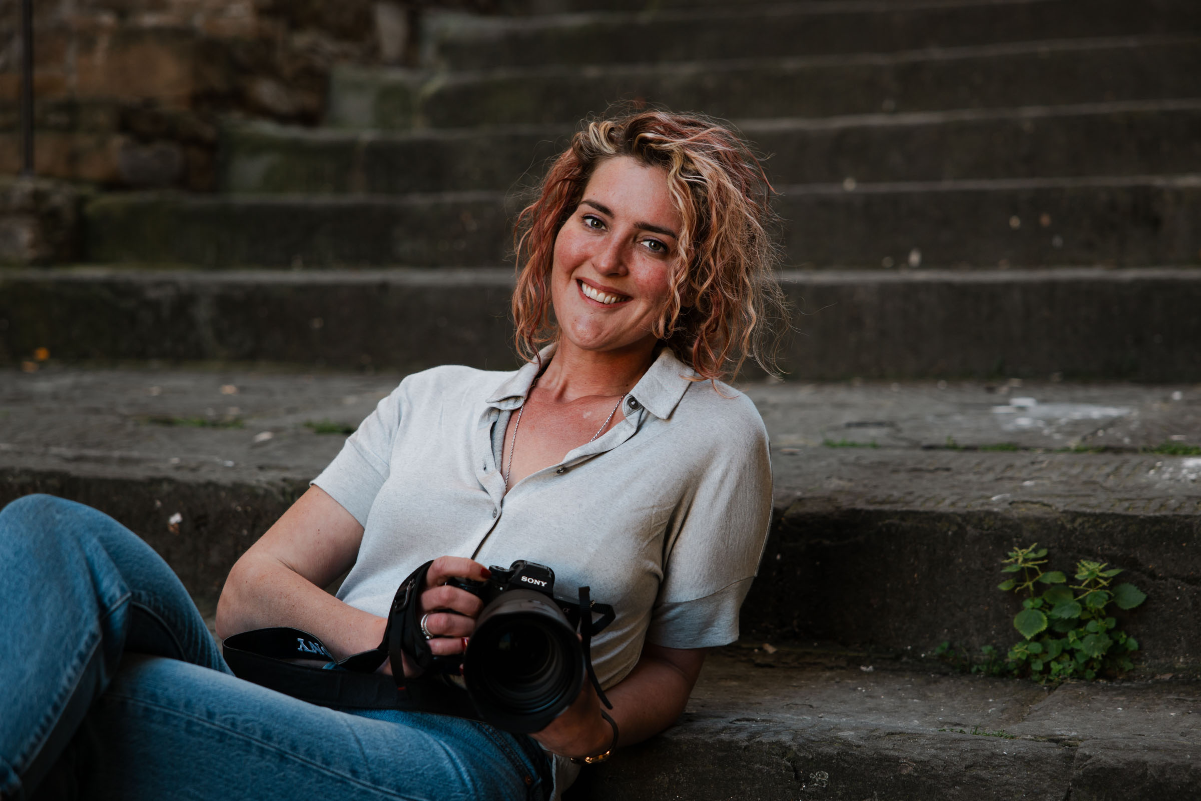 Sandra Koppelaar, documentair fotograaf uit Zeeland, lachend op een stenen trap met haar camera in Florence