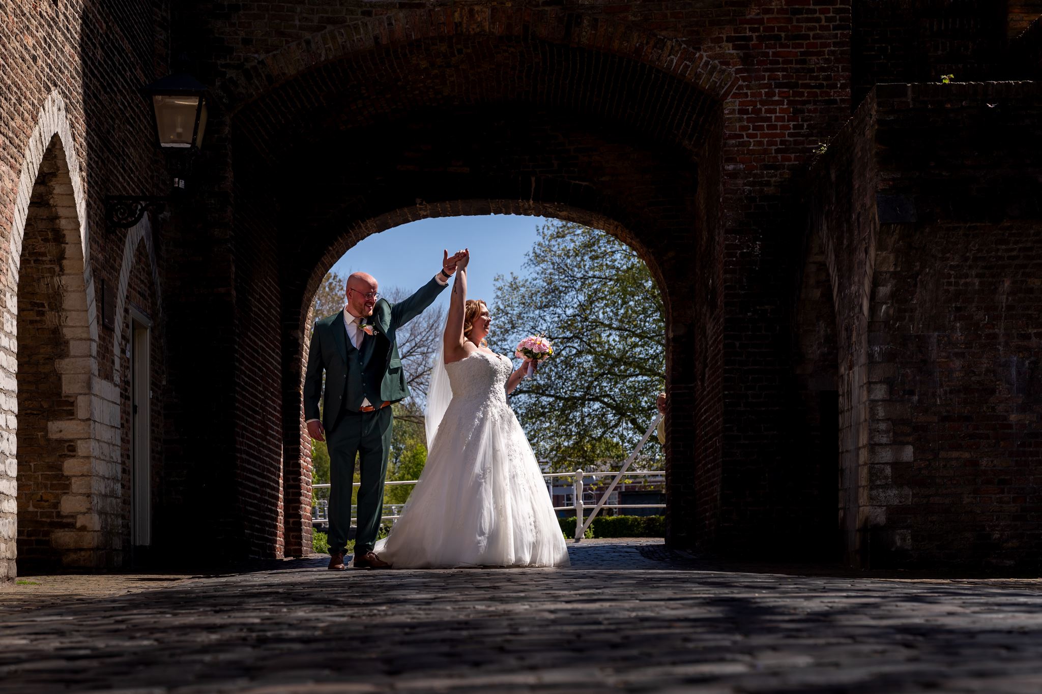 Bruidspaar loopt onder de oude stadspoort in Delft tijdens de fotoshoot, documentaire trouwfotografie