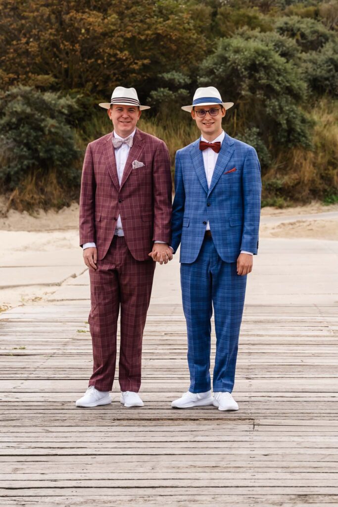 Twee bruidegoms in geruite pakken en hoeden op het strand van Renesse