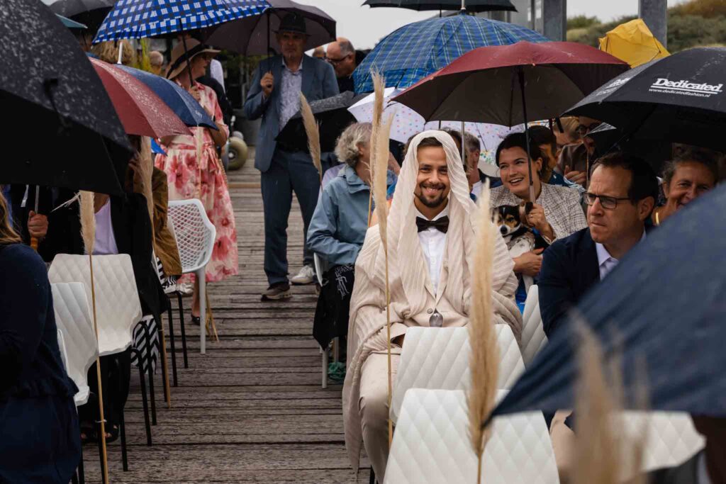 Gasten onder paraplu's tijdens de strandceremonie in de regen in Renesse