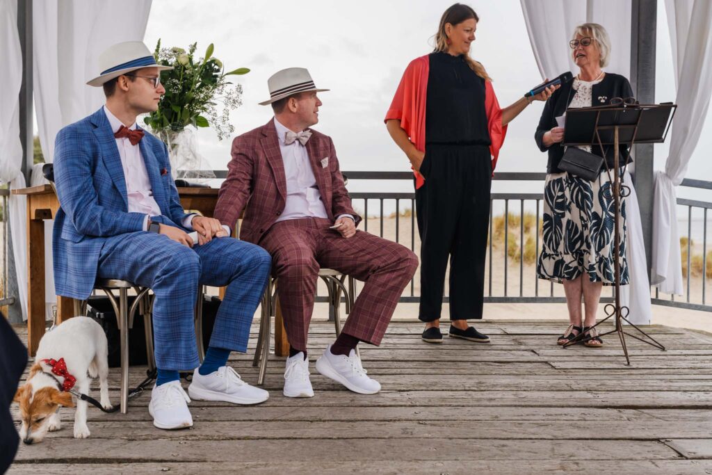 Bruidegoms luisteren naar een speech tijdens de ceremonie aan het strand van Renesse
