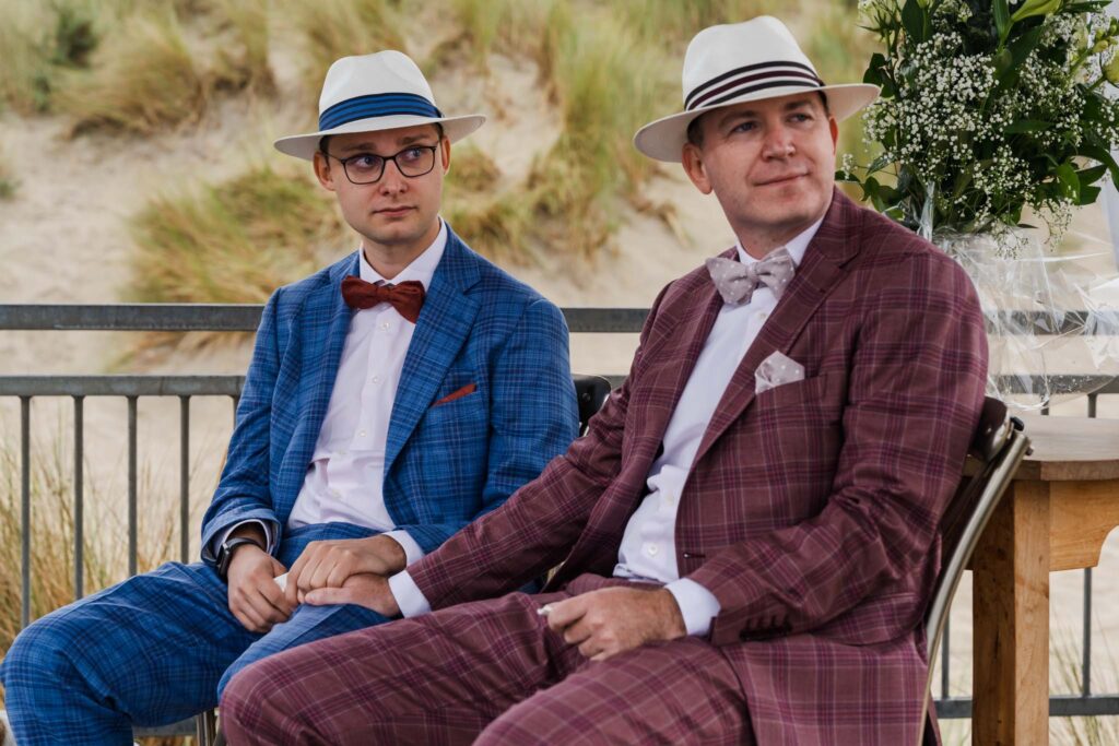 Bruidegoms lachen tijdens de ceremonie met de duinen van Renesse op de achtergrond