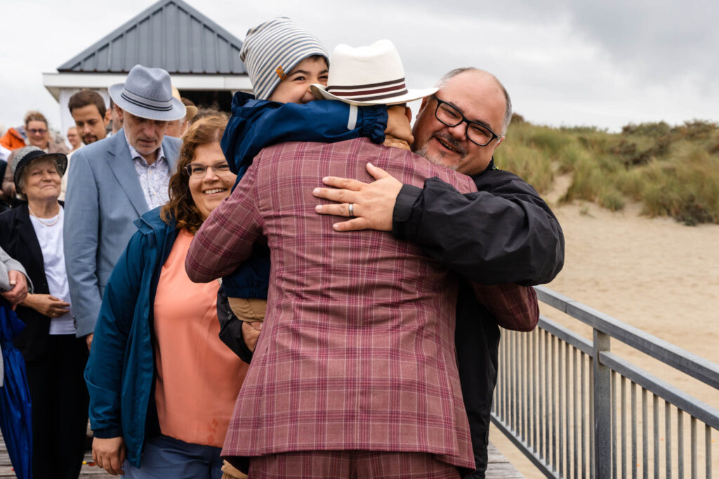 Bruidegom omhelst een gast tijdens de felicitaties aan het strand van Renesse