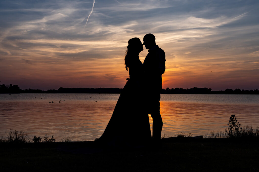 Silhouet van het bruidspaar bij zonsondergang aan het water in Valkenburg, documentaire trouwfotografie