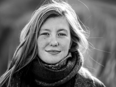 Zwart-witportret van een vrouw met een warme, directe blik tijdens een fotoshoot buiten in Zeeland, persoonlijke portretfotografie